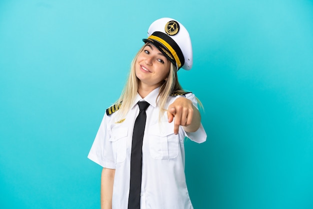 Airplane pilot over isolated blue background pointing front with happy expression