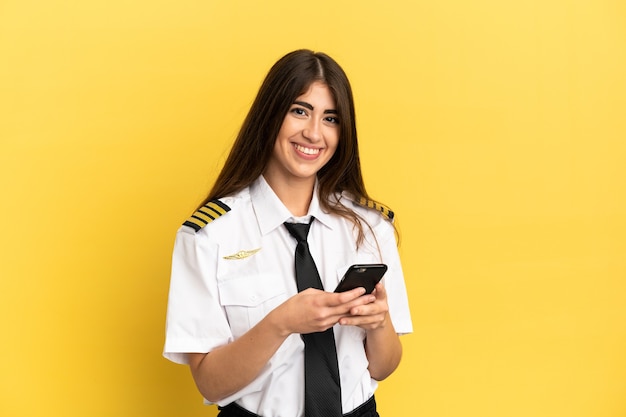 Airplane pilot isolated on yellow background sending a message with the mobile