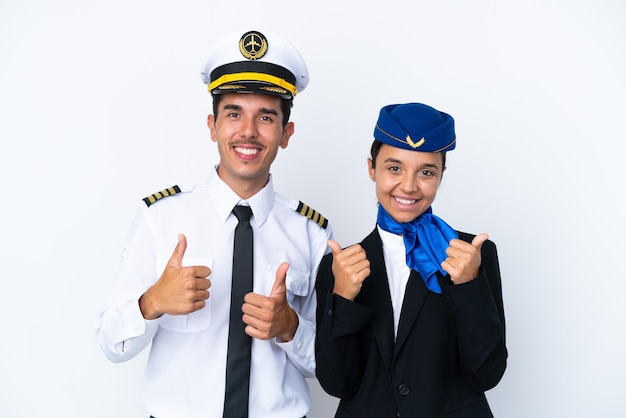 飛行機のパイロットと混血のエアホステスが白い背景で隔離され、両手で親指を立てて笑顔でジェスチャーをします
