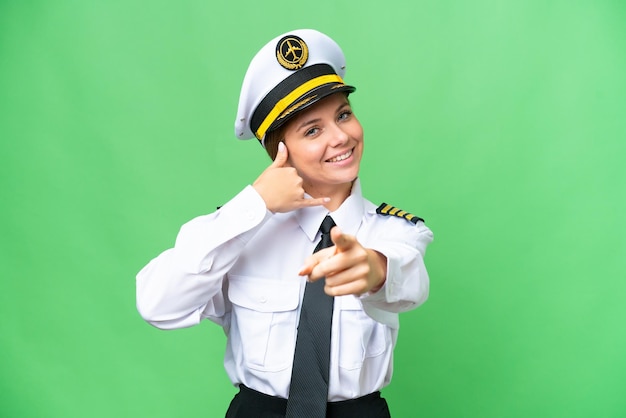 Airplane pilot woman over isolated chroma key background making phone gesture and pointing front