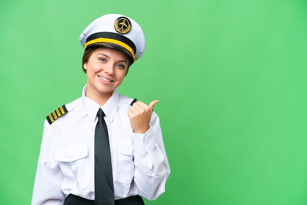 Airplane pilot woman over isolated chroma key background pointing to the side to present a product