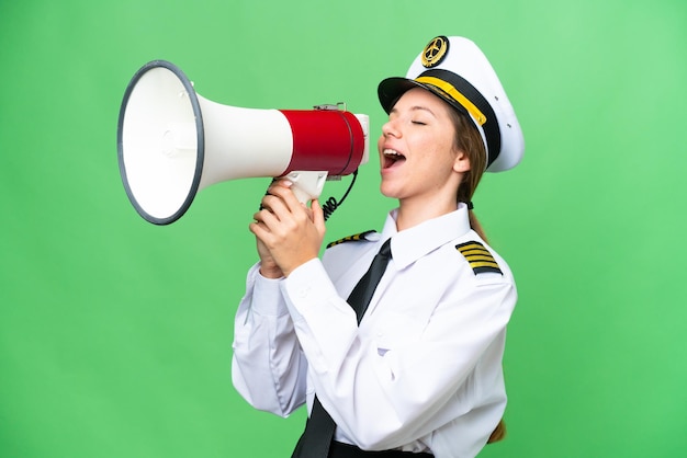 Airplane pilot woman over isolated chroma key background shouting through a megaphone