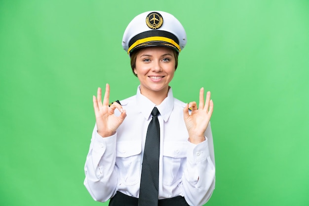 손가락으로 확인 표시를 보여주는 고립된 크로마 키 배경 위에 비행기 조종사 여자