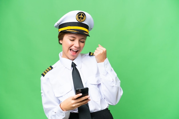 Airplane pilot woman over isolated chroma key background with phone in victory position