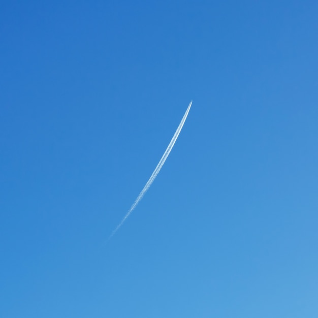 Airplane soaring in the blue sky, leaving a white vapor trail