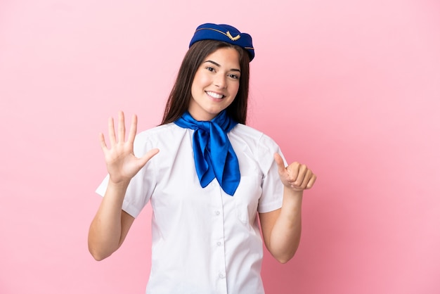 指で6を数えるピンクの背景に分離された飛行機のスチュワーデスブラジル人女性