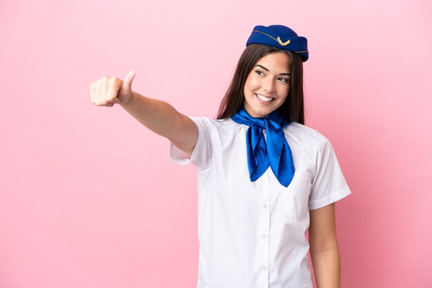 ピンクの背景に分離された飛行機のスチュワーデスブラジル人女性が親指を立てるジェスチャーを与える