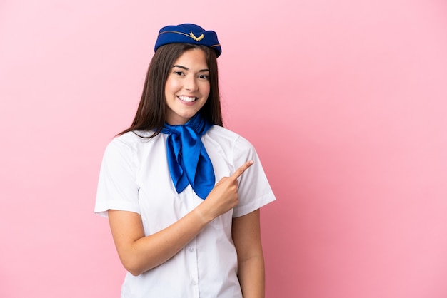 Airplane stewardess Brazilian woman isolated on pink background pointing to the side to present a product