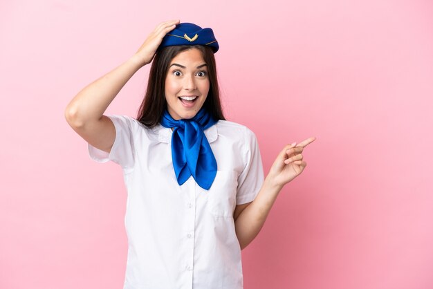 Airplane stewardess Brazilian woman isolated on pink background surprised and pointing finger to the side