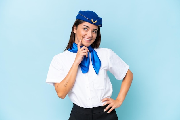 Airplane stewardess caucasian woman isolated on blue background thinking an idea while looking up