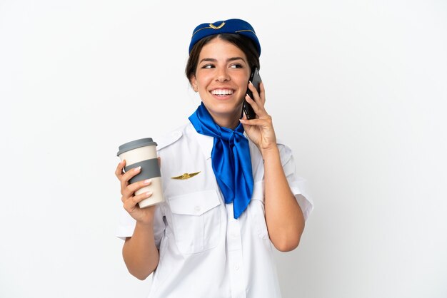持ち帰り用のコーヒーと携帯電話を保持している白い背景で隔離の飛行機スチュワーデス白人女性
