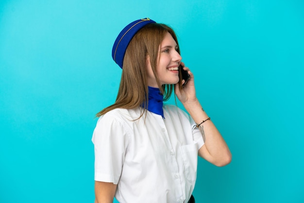 Airplane stewardess English woman isolated on blue background keeping a conversation with the mobile phone