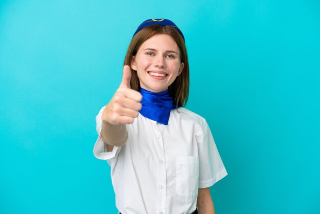 Hostess dell'aeroplano donna inglese isolata su sfondo blu con i pollici in su perché è successo qualcosa di buono