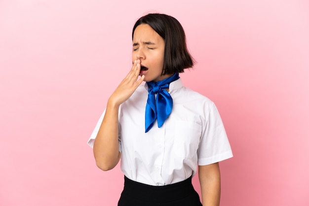 Airplane stewardess over isolated wall yawning and covering wide open mouth with hand