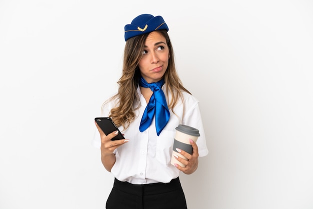 Airplane stewardess over isolated white background holding coffee to take away and a mobile while thinking something