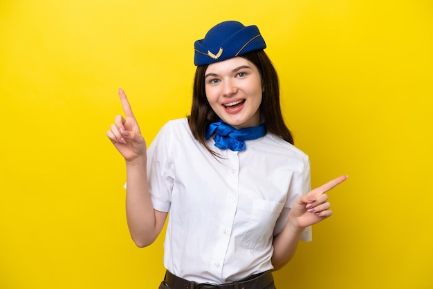 Airplane stewardess Russian woman isolated on yellow background pointing finger to the laterals and happy