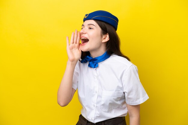 Airplane stewardess Russian woman isolated on yellow background shouting with mouth wide open to the lateral