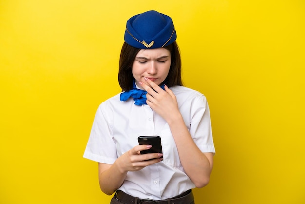 노란색 배경에 고립되어 생각하고 메시지를 보내는 비행기 스튜어디스 러시아 여성