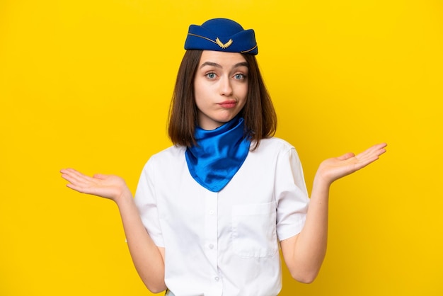 Foto hostess di aereo donna ucraina isolata su sfondo giallo che ha dubbi mentre alza le mani