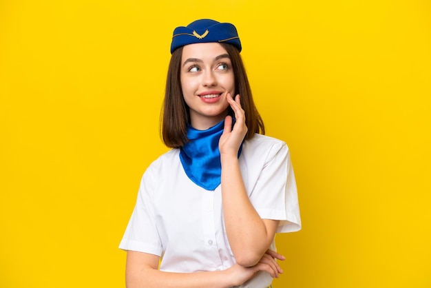 Airplane stewardess Ukrainian woman isolated on yellow background thinking an idea while looking up