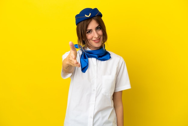 Airplane stewardess woman isolated on yellow background shaking hands for closing a good deal