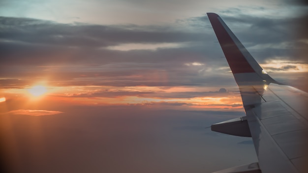 Airplane window view with wing at sunrise.