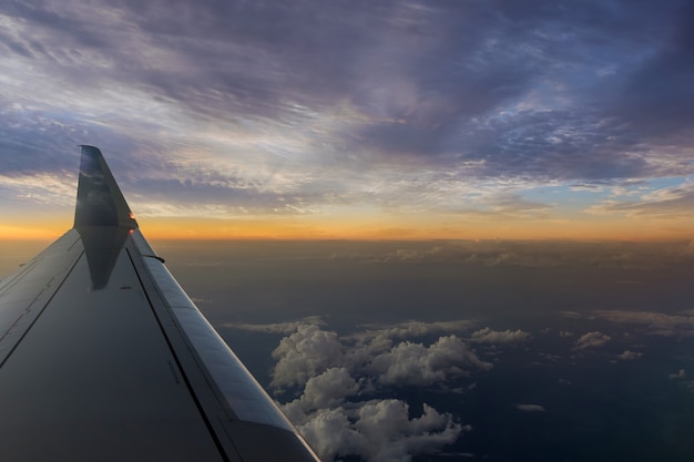 Airplane wing during flight at a wonderful sunset in fluffy clouds