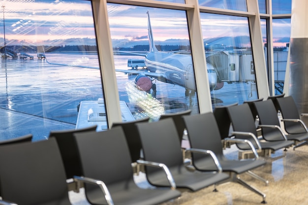 Area di attesa dell'aeroporto. aereo e cielo drammatico dietro le finestre. sedie vuote in una sala d'attesa in aeroporto