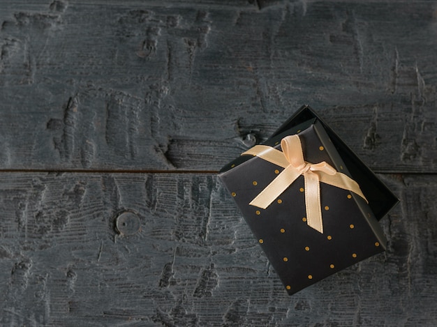 木製のテーブルに弓で半開きの黒いギフトボックス。