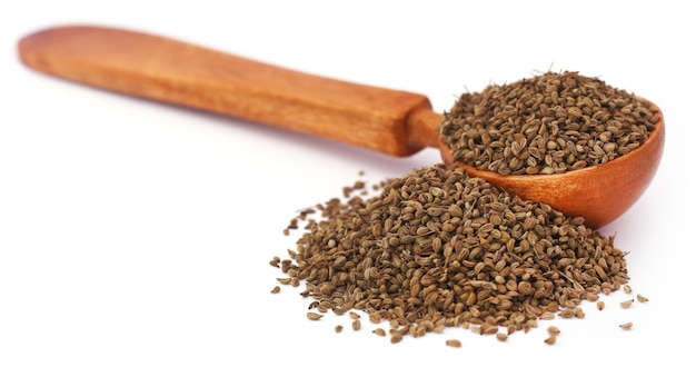 Ajwain seeds in a wooden spoon over white background