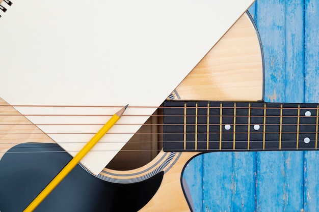 Akoestische gitaar op blauwe achtergrond het lichaamspatroon van de gitaar is houtnerf notebook en geel houten potlood