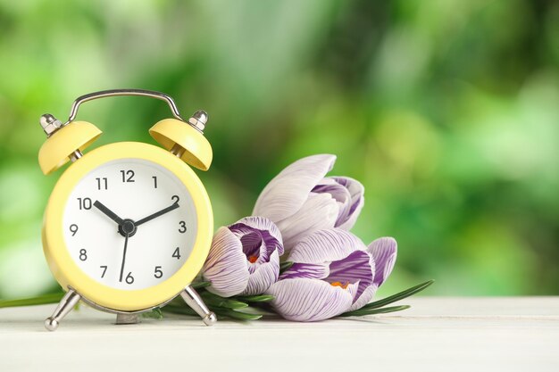 Alarm clock and beautiful spring flowers on white wooden table Time change concept