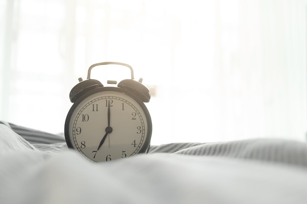 Alarm clock on bed in bedroom with morning sun light.