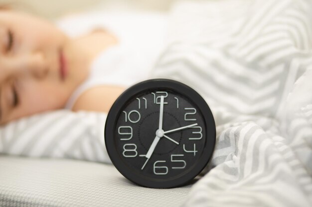 Foto orologio della sveglia sul letto ragazza carina che dorme sullo sfondo