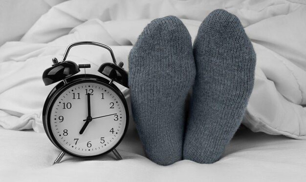 Alarm clock on bed next to female feet in socks