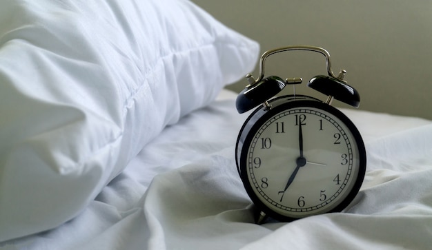 Alarm clock on the bed in hotel and pillow background