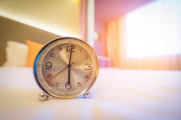 Alarm clock on the bed in morning time with sunlight.