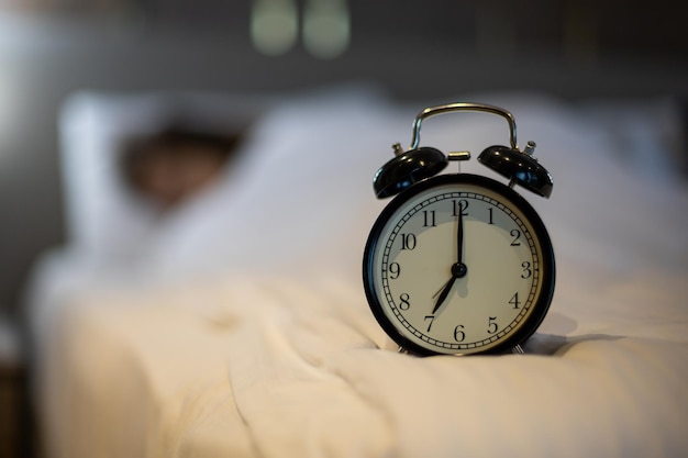 Alarm clock on the bed with sleeping woman behind