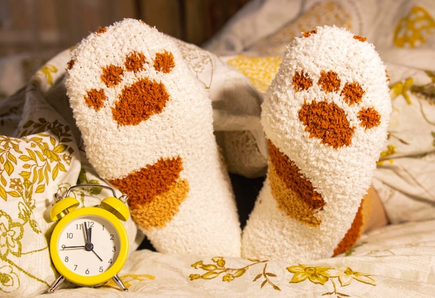 女性の足の横にあるベッドの目覚まし時計が、起きている間に毛布から突き出ている