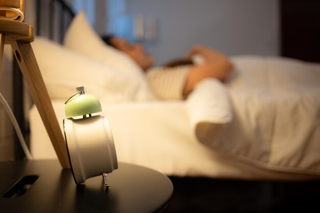 Alarm clock on a bedside table with woman sleeping in the background