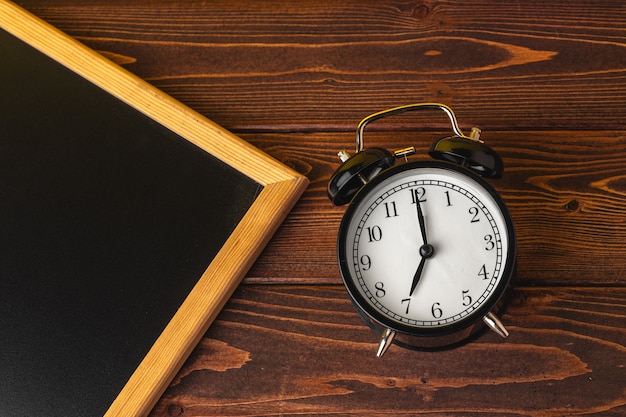 Alarm clock and blackboard on wooden table