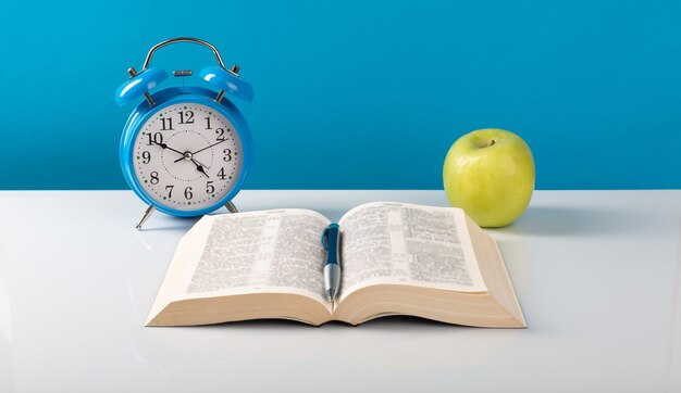 Alarm clock, book, apple on the table.