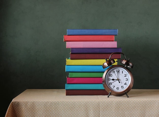 Alarm clock and books with colored covers on the table. Back to school.