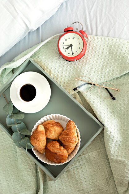 Alarm clock and coffee cup at bed in sunny room. Easy morning start, positive day beginning, waking up, new day, breakfast in bed concept. Flat lay, top view