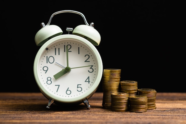 Alarm clock and coins stacks on working table in dark room