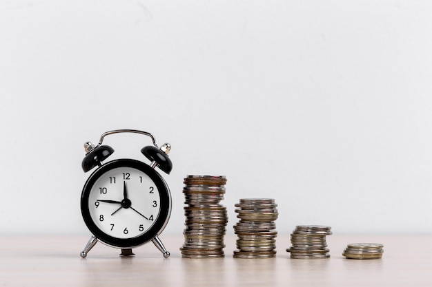 Alarm clock and coins on white surface