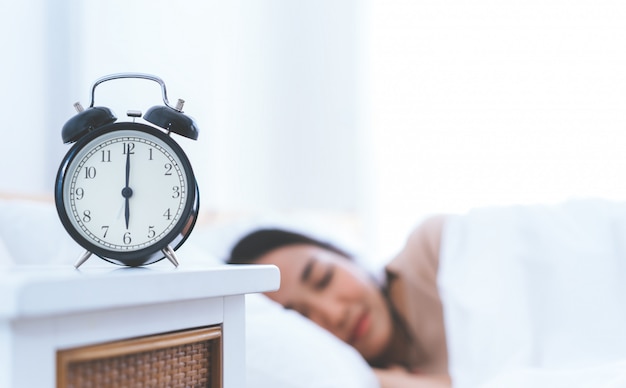 Alarm clock counting to six o clock with woman still sleeping in bed