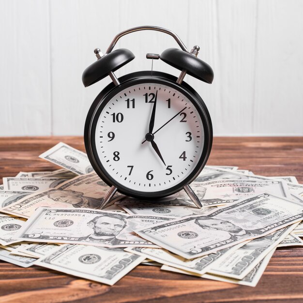 An alarm clock on currency notes over wooden table