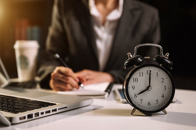 Alarm clock on the desk. Business working in modern office building or office at night using laptop.