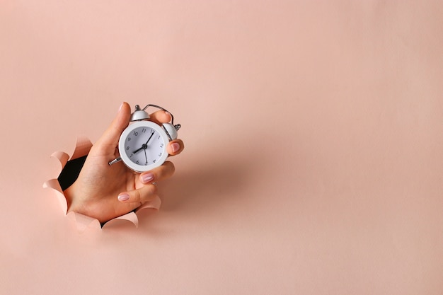 Alarm clock in a female hand holding through round hole in pink paper